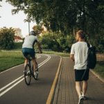 A cyclist and a walker enjoy a peaceful park trail surrounded by greenery.