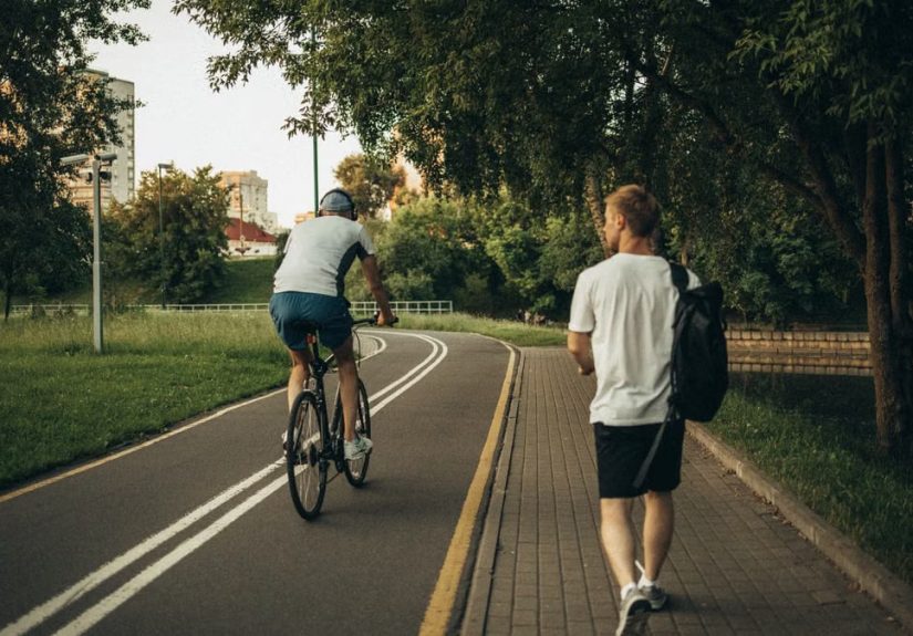 A cyclist and a walker enjoy a peaceful park trail surrounded by greenery.