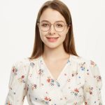 Young woman wearing glasses smiling in a floral outfit against a plain background.
