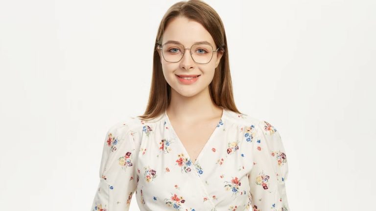 Young woman wearing glasses smiling in a floral outfit against a plain background.