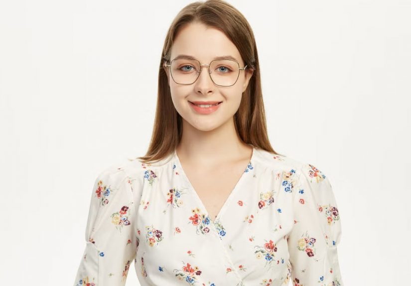 Young woman wearing glasses smiling in a floral outfit against a plain background.
