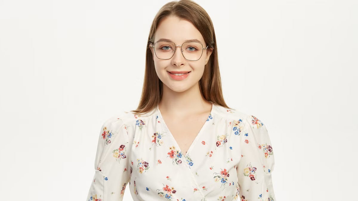 Young woman wearing glasses smiling in a floral outfit against a plain background.